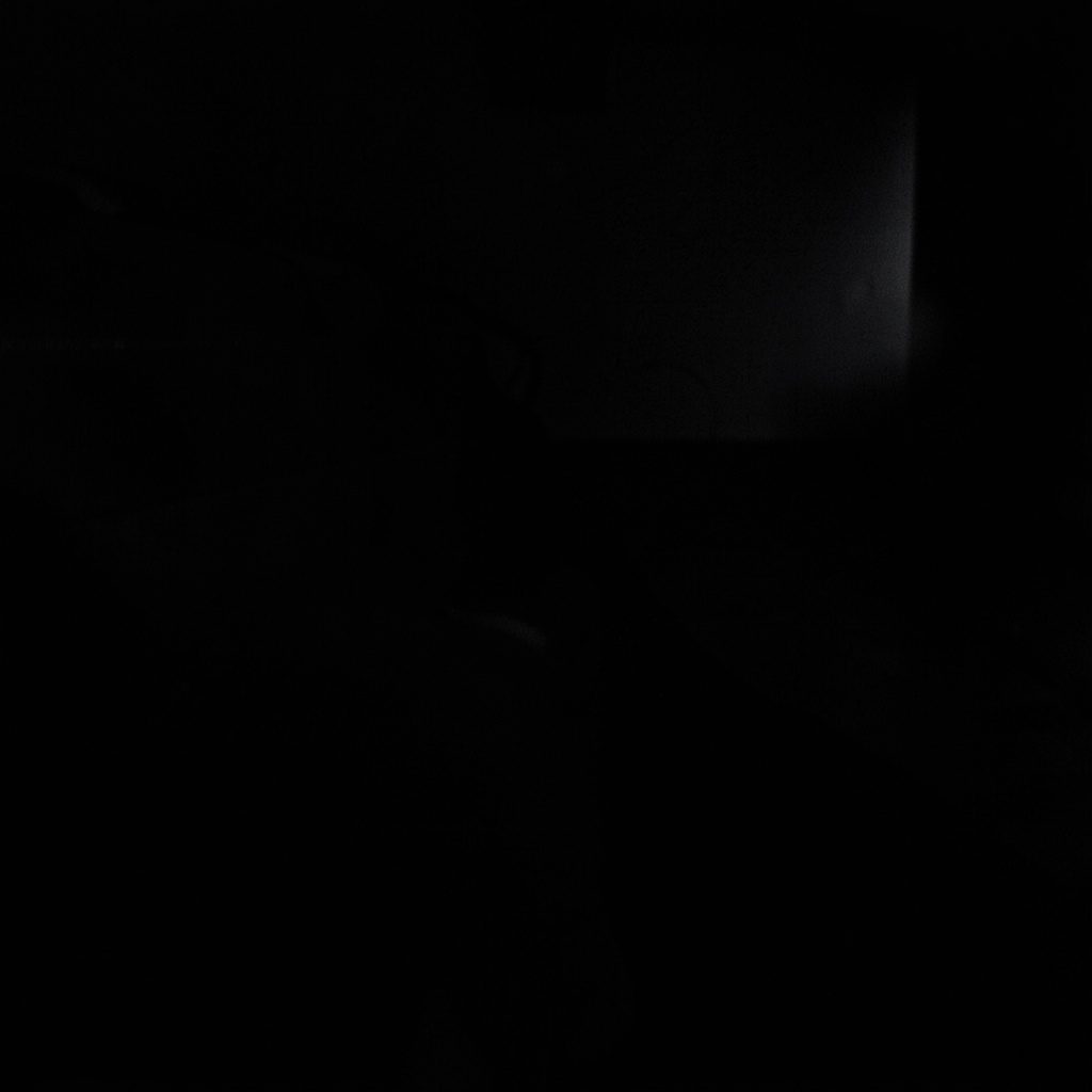 Dark, low-key photograph of a concert stage with deep shadows, moody blue and purple lighting, and silhouetted equipment.