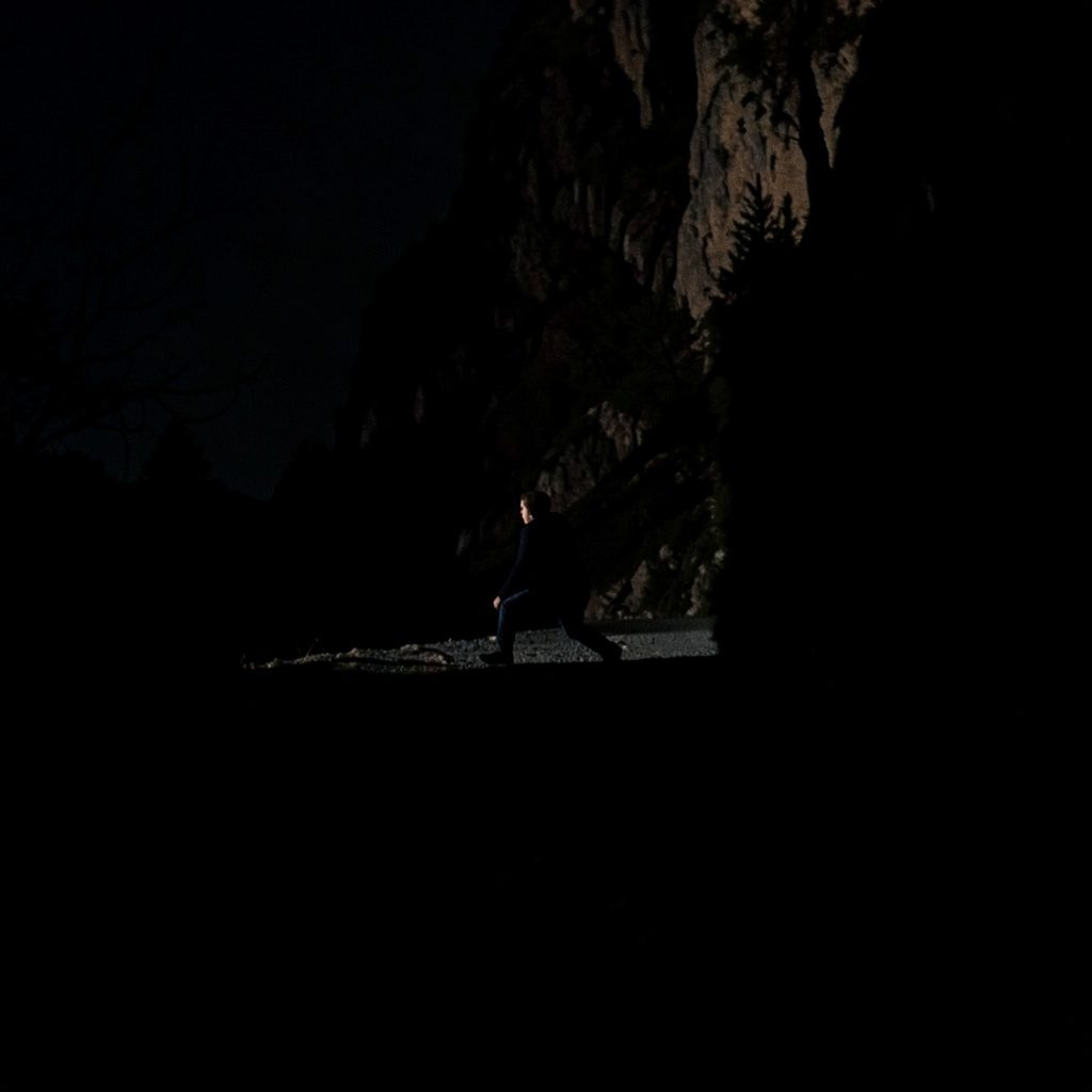 Dark atmospheric stage photograph with deep blue and purple lighting, a lone performer silhouette against moody concert haze.